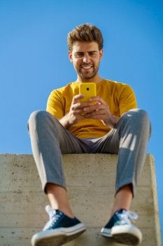 Young man using his smartphone sitting on a ledge outside. Man using his smartphone sitting on a ledge outside