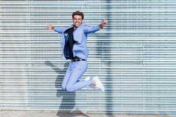 Young man wearing a suit jumping outdoors. Happy businessman in urban background.. Young man wearing a suit jumping outdoors