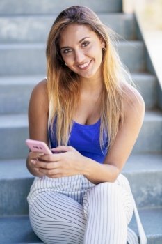 Young woman using a touchscreen smartphone wearing casual clothes. Girl sitting outdoors.. Girl using a touchscreen smartphone wearing casual clothes