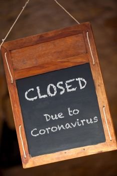 Traditional wooden blackboard or chalkboard sign hanging in a window saying Closed Due to Coronavirus