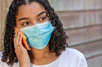 Mixed race African American teenager teen girl young woman wearing a face mask and talking on mobile cell phone during the Coronavirus COVID-19 pandemic