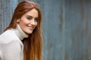 Outdoor portrait of beautiful girl or young woman with red hair smiling and happy in an urban city setting