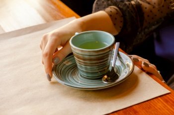 Vintage colors in the photo of hands and a cup of tea which stands on the table in front of a young girl who holds the bowl with her hand.. Vintage colors in hand photo and cups of tea on the table