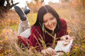 Happy woman lying down with book in the autumnal grass