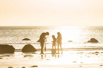 Children boy and girl playing with fisherman net on a beach. Sunset sea landscape with silhouette of people against sunset sky