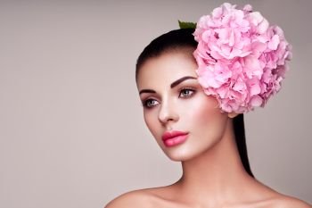 Portret model decorated with large pink flower on the head. Brunette woman with luxury makeup. Perfect skin. Eyelashes. Cosmetic eyeshadow