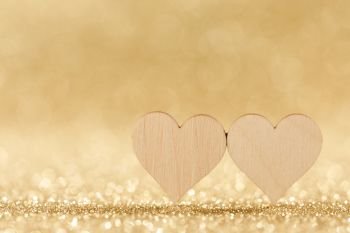 Two small handmade wooden hearts on bright golden lights bokeh background Valentines day card. Two hearts on bokeh background