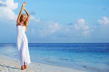 Young woman wearing a white dress standing on a beach and enjoying vacation. Woman in white on beach