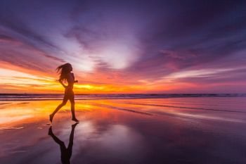 Picture of sexy female running on the beach, in a stylish bikini enjoying summer vacation at sunset copy space background. Woman running on beach at sunset