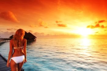 Happy young woman at beautiful water villa at Maldives island at sunset. Travel vacation tourist resort. Woman at water villa at Maldives island