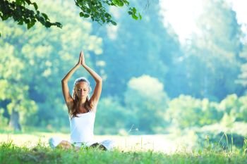 Yoga woman in white on green park grass in lotus asana pose. Yoga woman in park