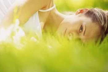 Young attractive blond woman is relaxing in the park laying in grass. Woman lay on grass
