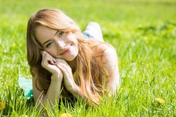 Happy smiling young woman laying on the green grass. Woman on the green grass