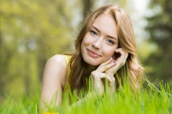 Happy smiling young woman laying on the green grass. Woman on the green grass