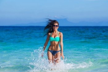Beautiful happy girl in bikini and sunglasses running in tropical sea waves. Girl running in sea waves