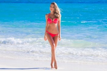 Beautiful young woman in sexy bikini standing at tropical sea beach. Young woman in red bikini