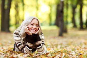 Portrait of young woman laying on ground with autumn leaves in park. Woman in autumn park