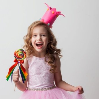 Beautiful excited candy princess girl in crown holding big lollipop and screaming of joy. Candy princess girl in crown