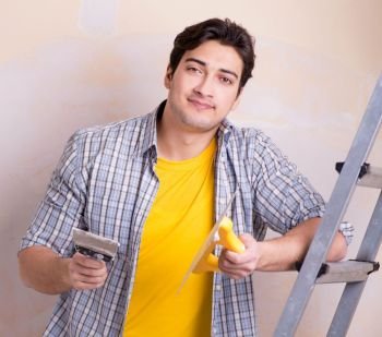 The young man applying plaster on wall at home. Young man applying plaster on wall at home