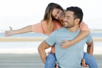 happy man giving woman piggyback on beach