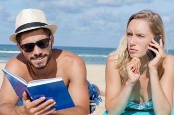 couple layed on beach man readying book woman on cellphone