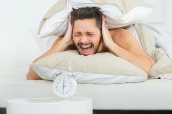 upset angry young man screaming at alarm clock on bedroom