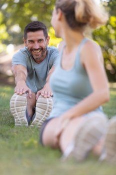 happy couple stretching while sitting on grass in the park