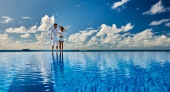Couple at infinity pool poolside against sky 