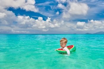 Three year old toddler boy on beach at Seychelles swimming with inflatable ring