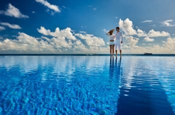 Couple at infinity pool poolside against sky 