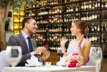 proposal, couple and valentine’s day concept - excited young woman looking at man with engagement ring over restaurant or wine bar background. man making proposal to happy woman at restaurant