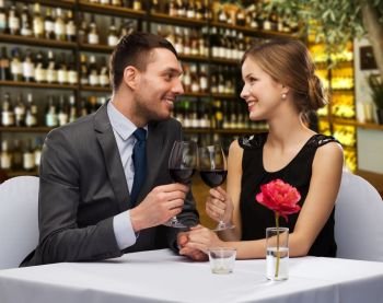 valentine’s day, leisure and luxury concept - smiling couple clinking glasses of red wine over restaurant background. happy couple drinking red wine at restaurant
