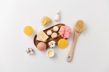 beauty, spa and wellness concept - close up of konjac sponge, crafted soap bars on wooden tray and body butter with natural bristle brush. crafted soap, sponges, brush and natural cosmetics