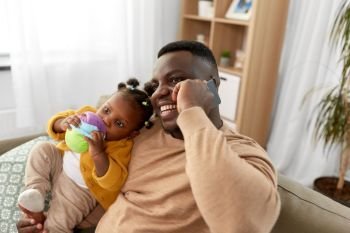 family, fatherhood and technology concept - happy african american father with baby at home calling on smartphone. father with baby at home calling on smartphone