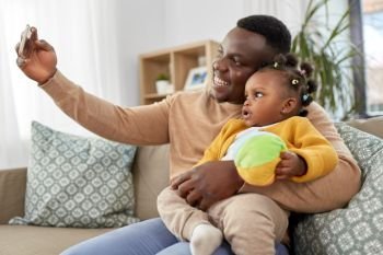 family, fatherhood and people concept - happy african american father with little baby daughter taking selfie by smartphone at home. happy father with baby taking selfie at home