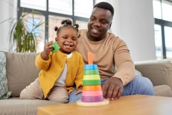 family, parenthood and people concept - happy african american father and baby daughter playing with toy blocks at home. african family playing with baby daughter at home