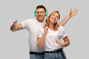 music, technology and people concept - portrait of happy couple in white t-shirts and headphones dancing over grey background. happy couple in headphones dancing