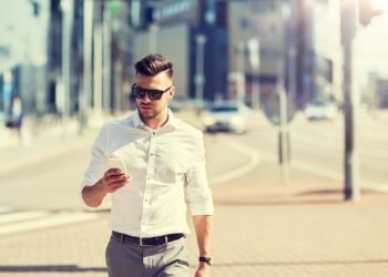 business, technology, communication and people concept - young man in sunglasses with smartphone walking in city. man in sunglasses with smartphone walking at city
