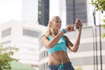 fitness, sport and people concept - smiling young woman with smartphone and earphones listening to music and exercising over city street on background. happy woman with smartphone and earphones at city