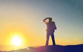 travel, tourism, hike and people concept - traveller with backpack standing on edge of hill and looking far away over sunrise background. traveller looking far away over sunrise