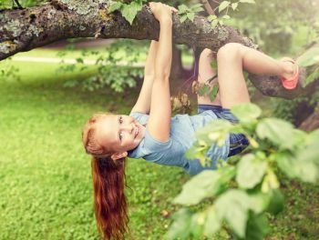 friendship, childhood, leisure and people concept - happy smiling little redhead girl hanging upside down on tree in summer park. happy little girl hanging on tree in summer park