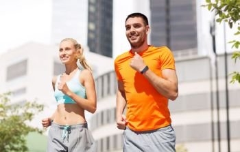 sport, healthy lifestyle and people concept - smiling couple with fitness trackers running at summer over city street on background. happy couple with fitness trackers running at city