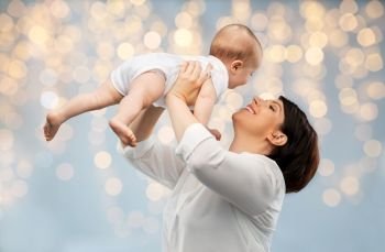 family, child and parenthood concept - happy smiling middle-aged mother holding little baby daughter over festive lights background. happy middle-aged mother with little baby daughter