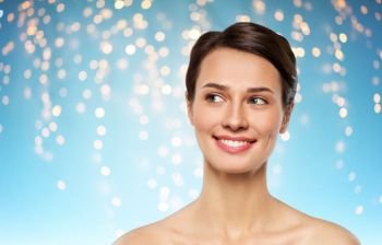 beauty, bodycare and people concept - beautiful smiling young woman with bare shoulder over holidays lights on blue background. beautiful smiling young woman with bare shoulder