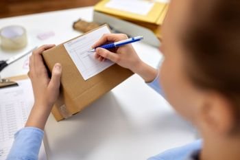 delivery, mail service, people and shipment concept - close up of woman filling postal form on parcel box at office. close up of woman filling postal form at office