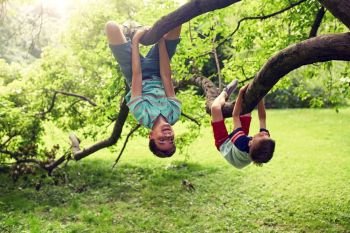 friendship, childhood, leisure and people concept - two happy kids or friends hanging upside down on tree and having fun in summer park. two happy boys hanging on tree in summer park