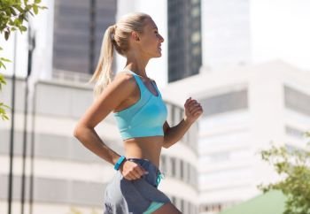 sport, healthy lifestyle and people concept - smiling young woman with fitness tracker running over city street on background. smiling young woman running at city