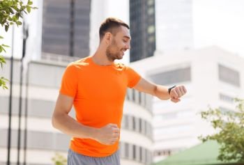 sport, technology and people concept - smiling young man with smart watch or fitness tracker running in summer over city street on background. smiling young man with smart watch running at city