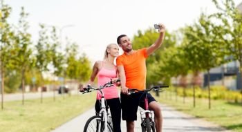 fitness, sport and people concept - happy couple with bicycles taking selfie by smartphone over city street on background. couple with bicycles taking selfie by smartphone