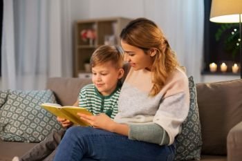 family, leisure and people concept - happy smiling mother and little son reading book sitting on sofa at home. happy mother and son reading book sofa at home
